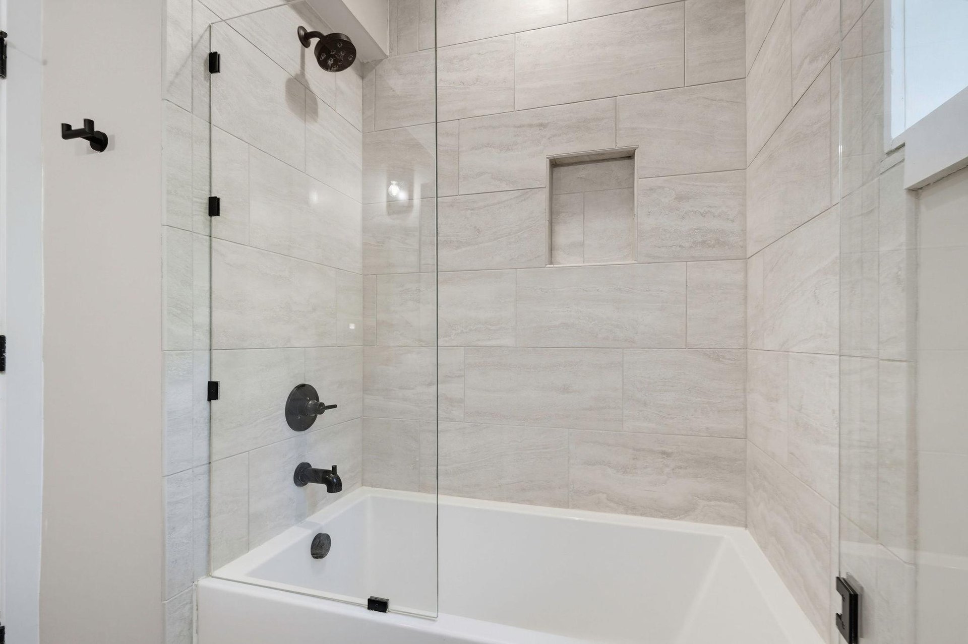 Step into a beautifully appointed bathroom featuring light stonetiled walls and modern fixtures with sleek black hardware. The glassenclosed tubshower combo offers both elegance and functionality f