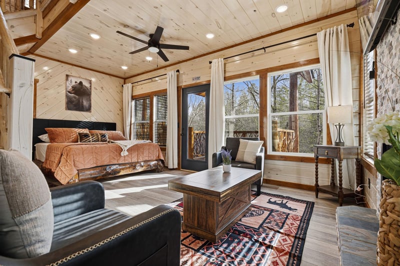 Wake to forest views through your wall of windows in this luxurious cabin bedroom with cozy sitting area.