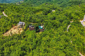 Aerial view of the property nestled among lush forested mountains, offering a serene mountain retreat setting surrounded by natural landscape and winding roads.