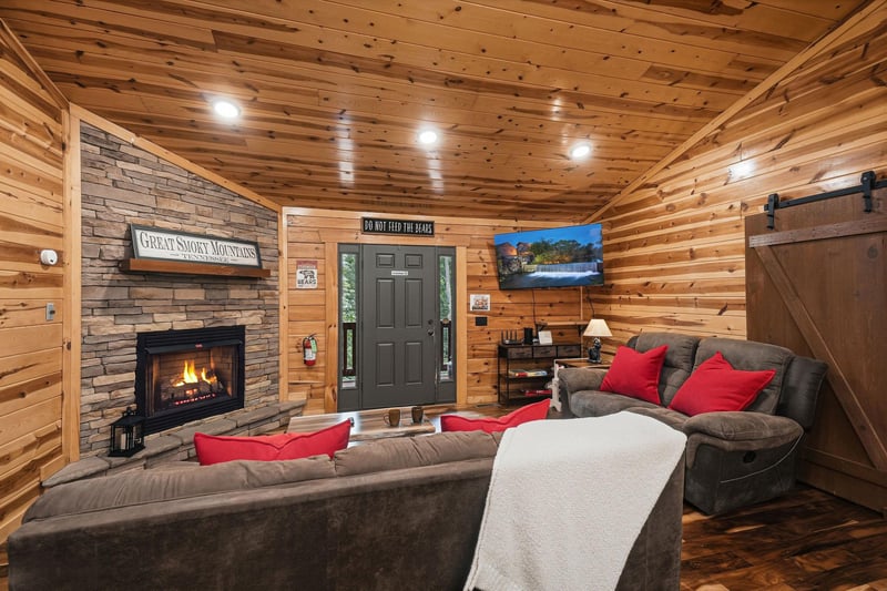 Sink into plush sofas beside a stone fireplace in this warm, woodpaneled living room. Rustic barn doors and mountaininspired charm create your perfect cozy retreat.