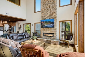 Settle into plush seating before your dramatic stone fireplace, where vaulted ceilings and floortoceiling windows frame peaceful greens beyond.