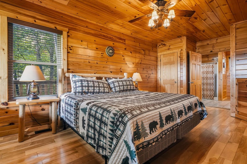Step into your cozy cabin bedroom with rich woodpaneled walls and a rustic chandelier overhead. A plush bed awaits, dressed in charming plaid and bearpatterned linens that invite restful mountain ni