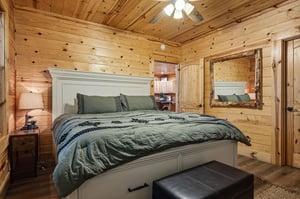 Your cozy mountain bedroom invites you to sink into plush bedding beneath knotty pine walls, with rustic log accents and warm cabin charm creating your perfect retreat.
