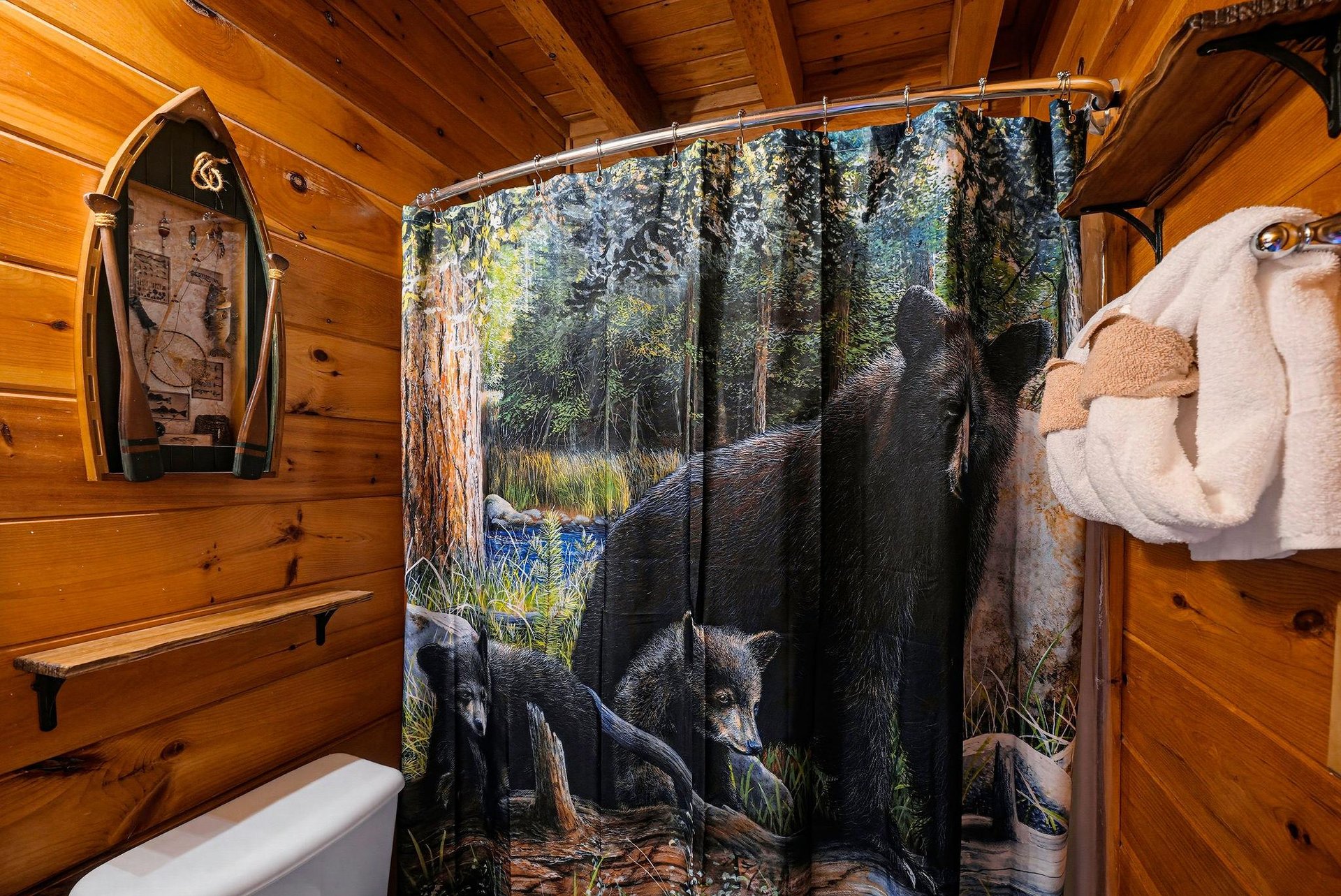 Rustic cabin bathroom with warm wood paneling, a whimsical bear shower curtain, and a playful fish sculpture adding character to your mountain retreat.