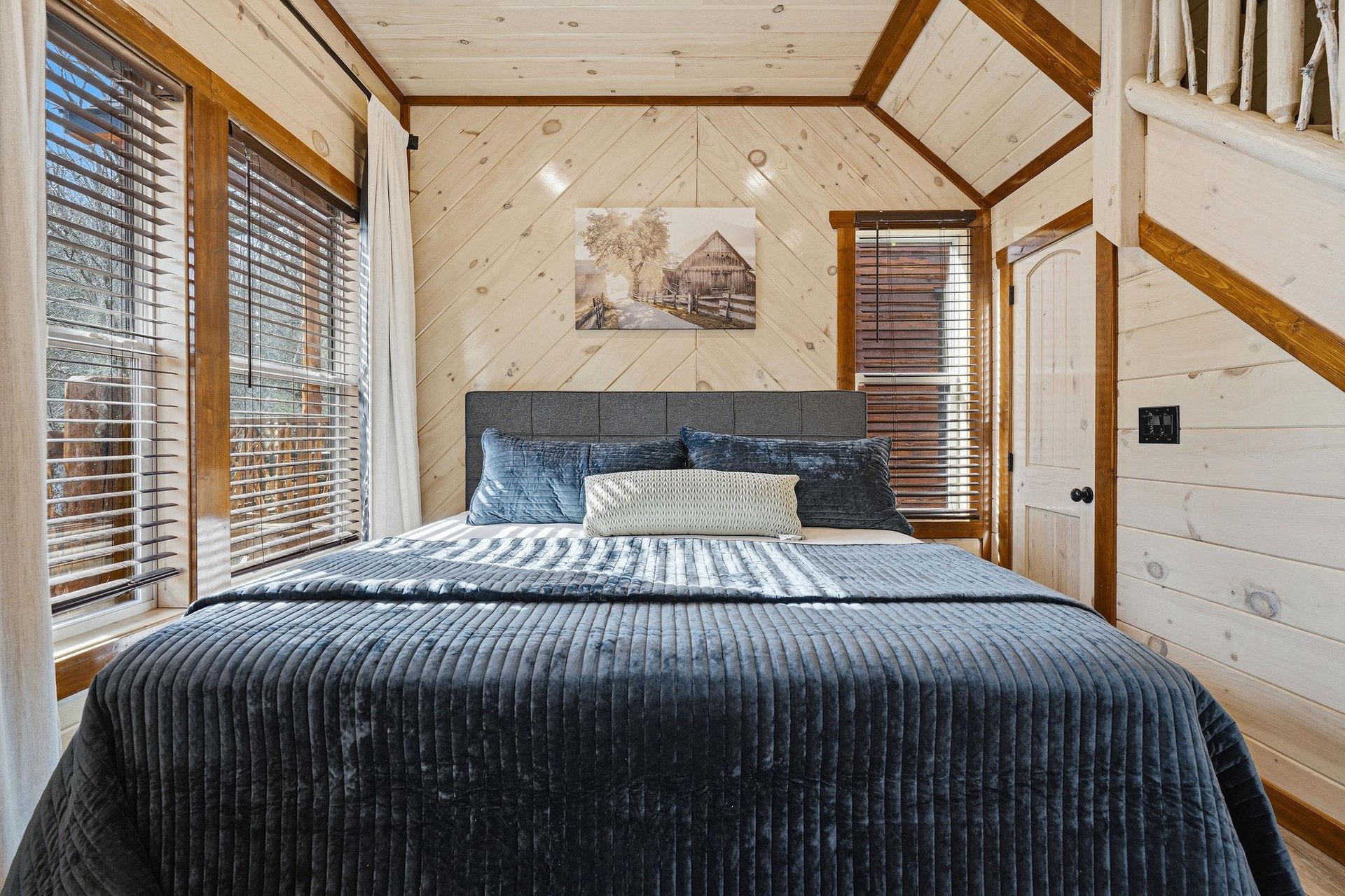 Drift off in your cozy cabin bedroom, wrapped in rich navy linens beneath soaring woodbeamed ceilings that create an intimate mountain retreat atmosphere.