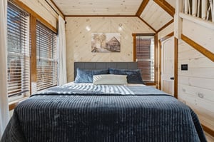 Drift off in your cozy cabin bedroom, wrapped in rich navy linens beneath soaring woodbeamed ceilings that create an intimate mountain retreat atmosphere.