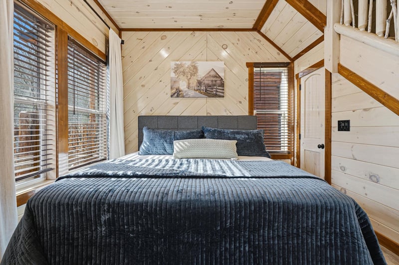 Drift off in your cozy cabin bedroom, wrapped in rich navy linens beneath soaring woodbeamed ceilings that create an intimate mountain retreat atmosphere.
