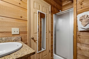 Step into your cozy cabin bathroom with warm wood walls, a granite countertop, and a refreshing shower ready for you after a day of adventure.