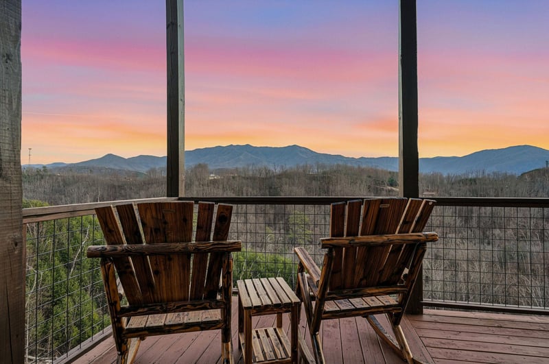 Mountain sunset paints the sky in brilliant colors beyond the balcony, creating a stunning backdrop for the surrounding landscape.