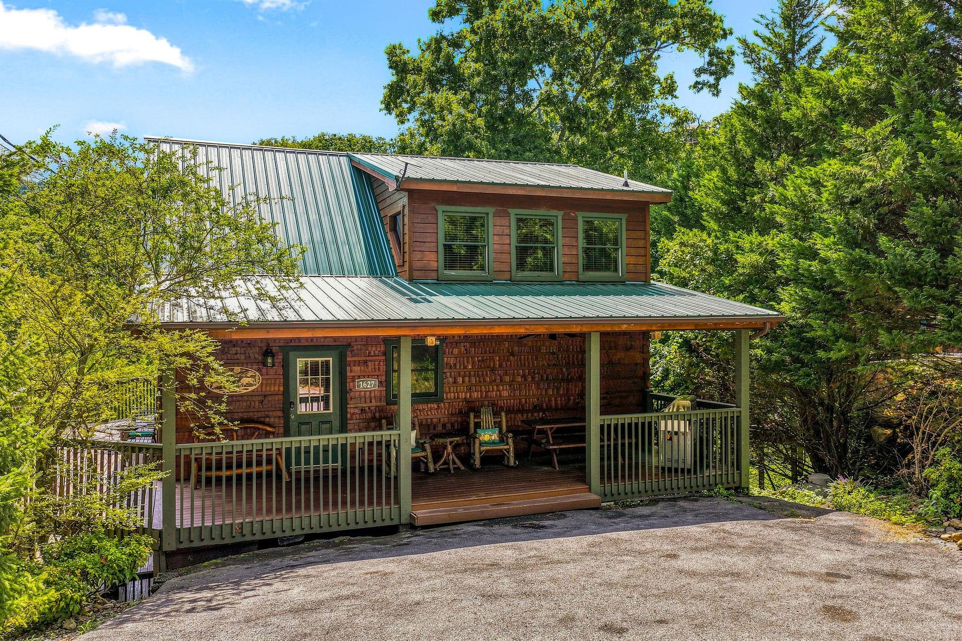 A charming twostory cabin nestled among towering trees, featuring rustic wood siding and a welcoming covered front porch with seating, offering a peaceful wooded retreat.