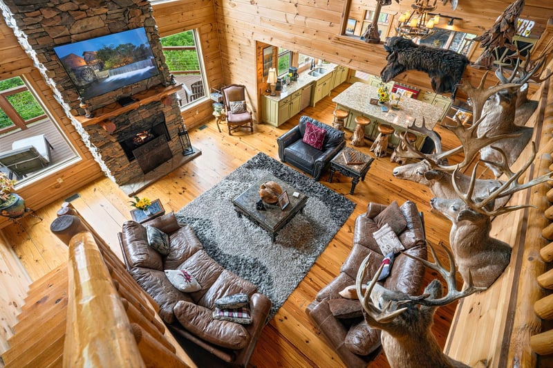 Your cozy rustic retreat features a dramatic stone fireplace, plush leather seating, and a chefs kitchen—all framed by soaring log beam architecture and natural light from vaulted windows.