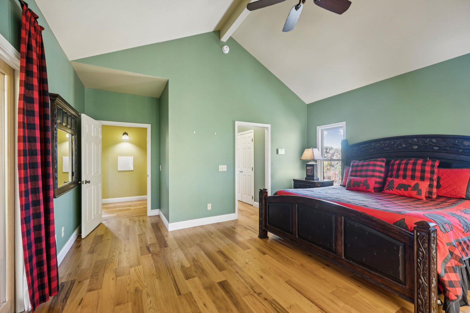 Youll love the spacious primary bedroom with vaulted ceilings, warm hardwood floors, and striking redandblack plaid bedding. Natural light and soothing sage walls create the perfect retreat for res