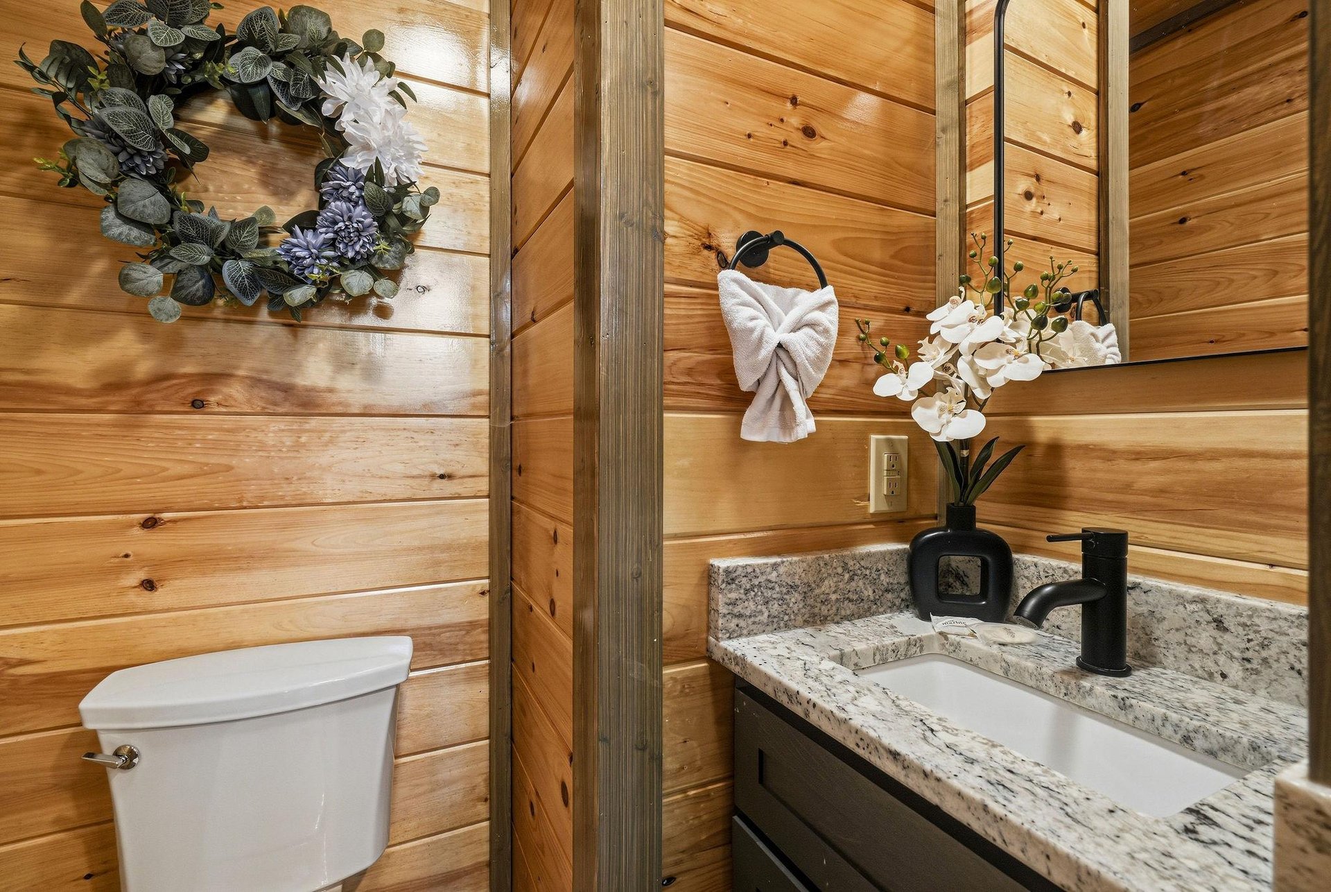 Youll love this charming bathrooms warm wood walls and granite vanity, perfectly appointed with elegant towel art and fresh orchids.