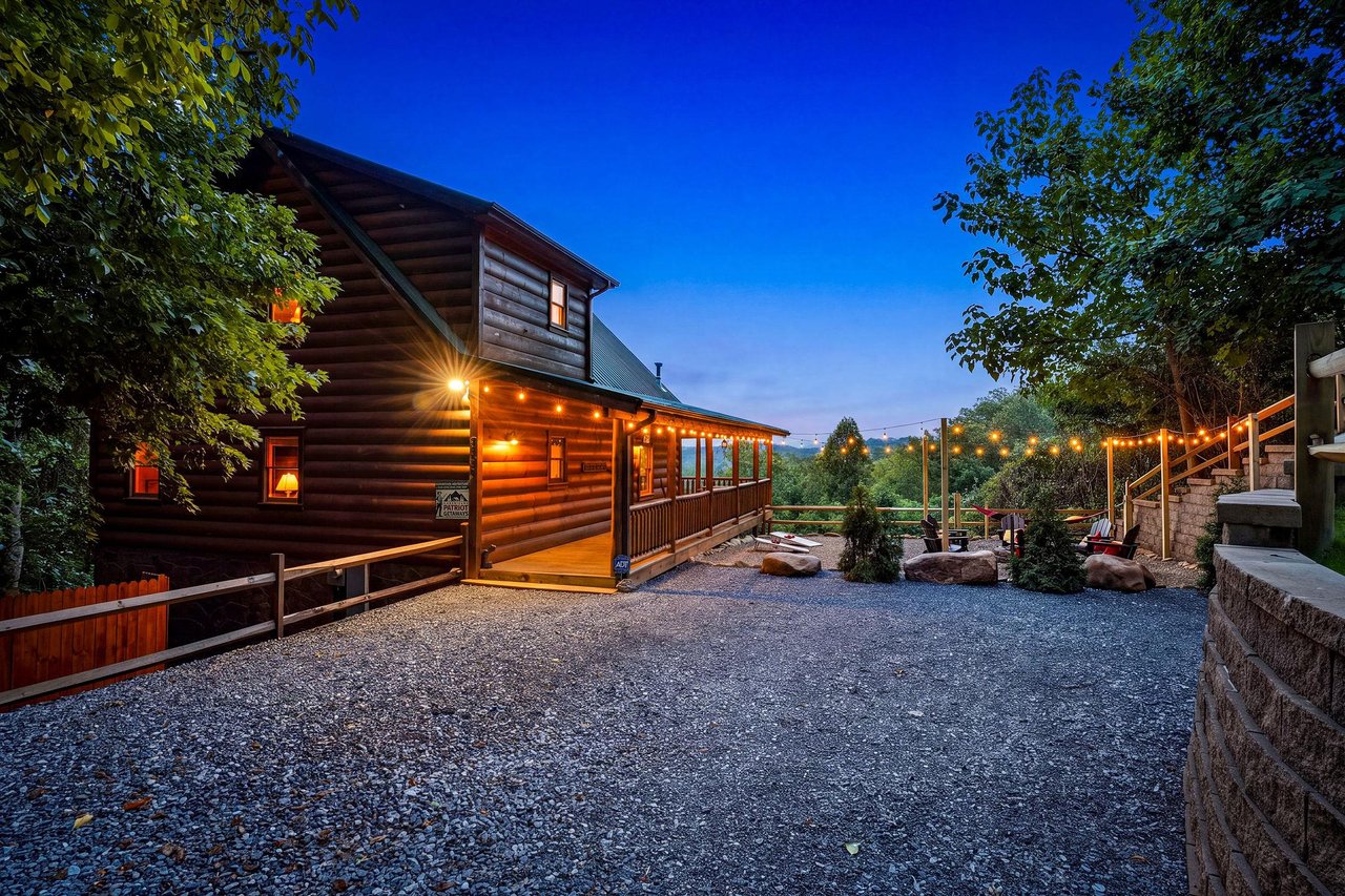 This charming log cabin property sits nestled among trees with welcoming outdoor lighting and a spacious gravel parking area, offering a cozy mountain retreat surrounded by natural beauty.