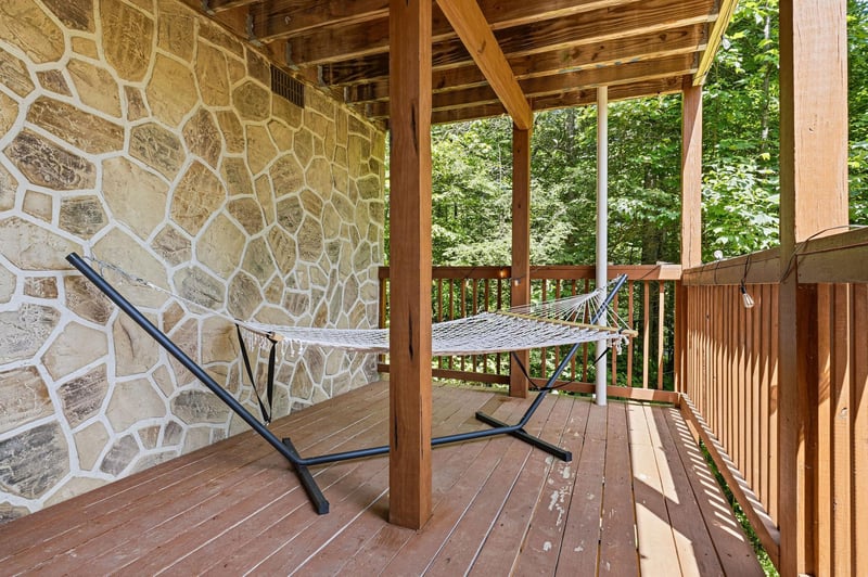 Swing gently in your hammock beneath a rustic wooden ceiling, stone wall at your back, and lush green forest just beyond the railing.