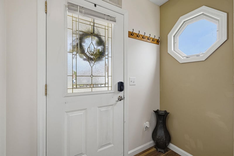 A welcoming entrance greets arrivals, featuring decorative stained glass, a charming wreath, and practical hooks for jackets and bags. Natural light streams through the unique octagonal window above.