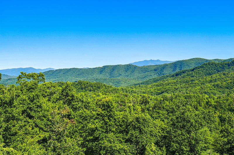 Stunning mountain panorama with rolling forested ridges stretching to the horizon under a clear blue sky, part of the scenic area surrounding the property.