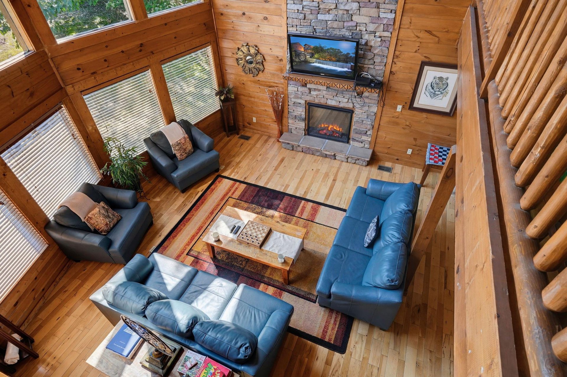 Soaring windows frame forest views in this cozy log cabin living room. Sink into plush seating by the stone fireplace and let the natural light and warmth embrace your mountain retreat.