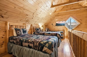 Your cozy log cabin loft features rustic twin beds with charming woodland quilts, creating the perfect mountain retreat atmosphere.