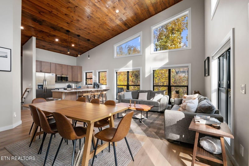 Step into an open, airy retreat where soaring ceilings with rich wood planks draw your eyes upward. Sunlight pours through floortoceiling windows, framing vibrant autumn views that make every moment