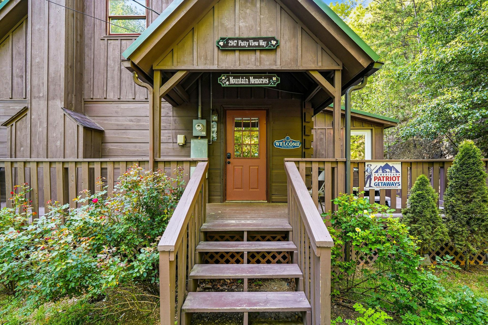 Charming mountain cabin entrance with rustic wood siding and welcoming front steps surrounded by lush greenery.