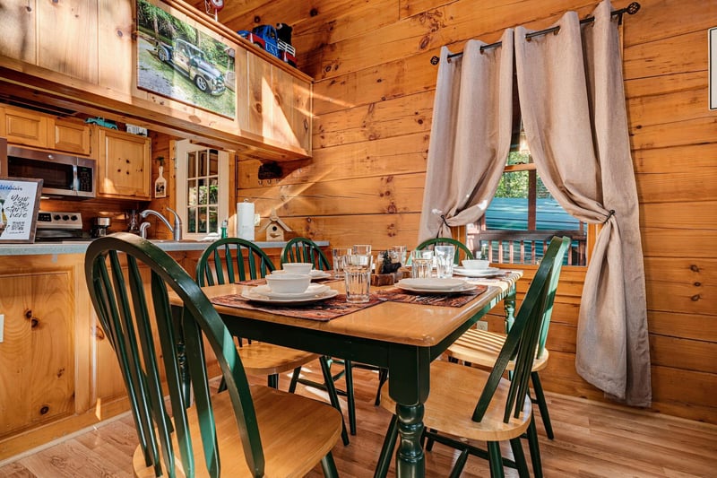 Gather around the charming farmhouse table for a meal bathed in natural light, surrounded by warm knotty pine walls that create a cozy cabin atmosphere perfect for your mountain getaway.