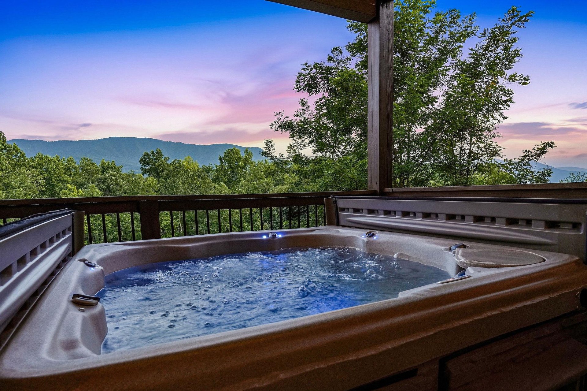 Soak in the private hot tub on your covered deck as the sky shifts into pastel hues at dusk, with rolling mountain ridges and lush forest creating a serene, secluded backdrop.
