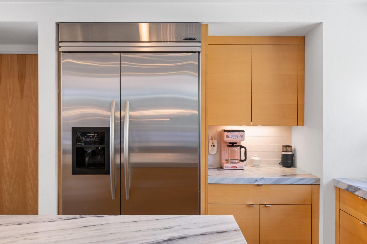 Modern chefs kitchen with a waterfall marble counter, kitchen island, stainlesssteel appliances, wine fridge, wet bar, and kitchen essentials.