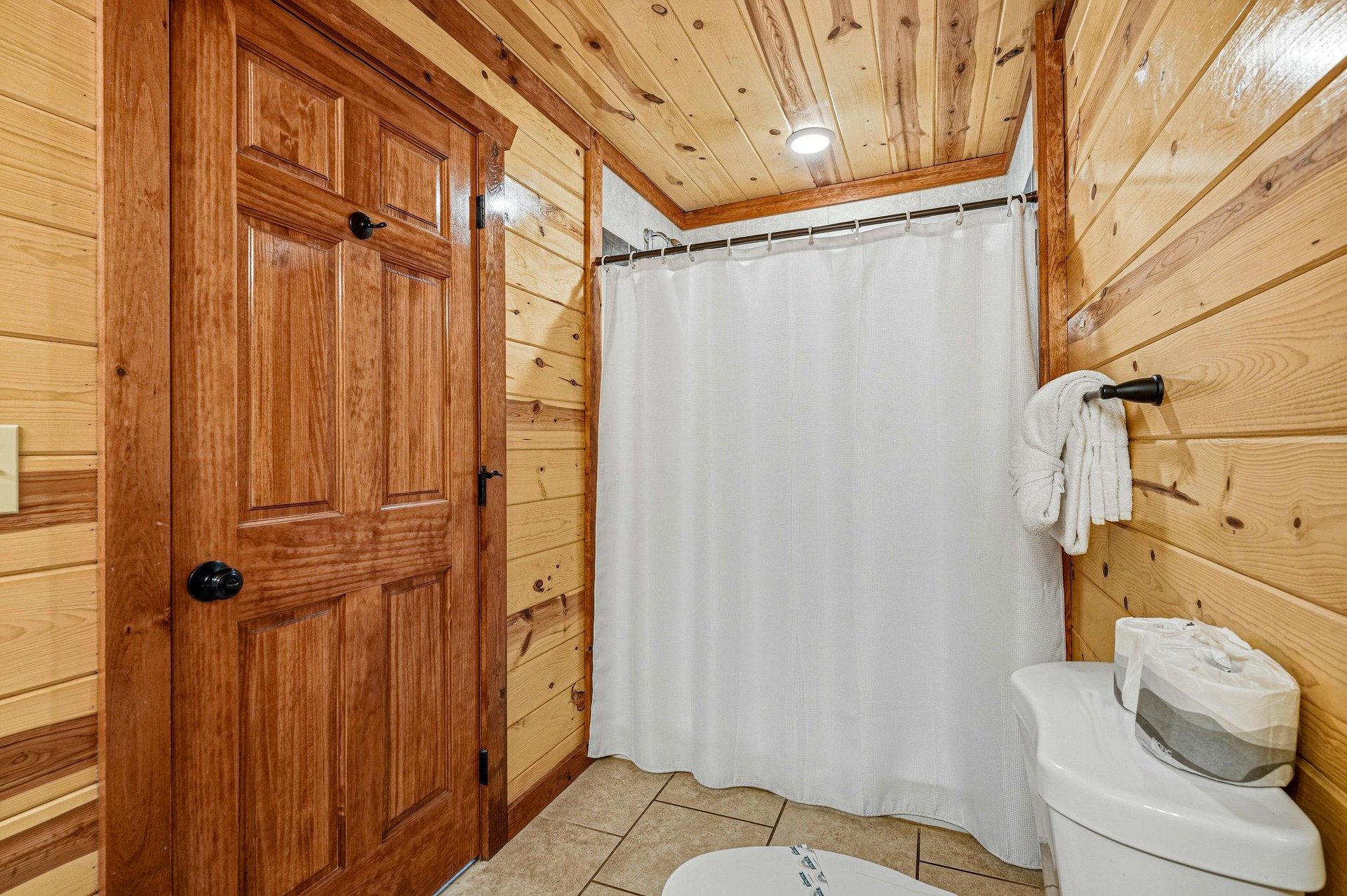 Step into your rustic bathroom where warm wood walls create a cozy cabin atmosphere, complete with fresh towels and everything you need to refresh.