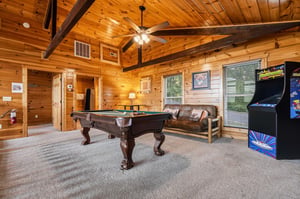 Your private game room awaits with rich wood beams, a fullsize pool table, classic arcade games, and a cozy leather sofa—perfect for friendly competition and unforgettable evenings.