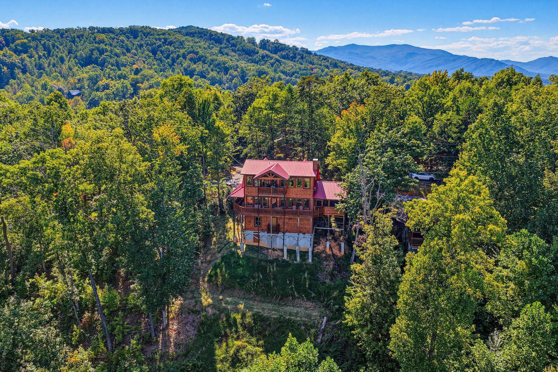 A striking mountain cabin set among lush forest with dramatic Blue Ridge peaks stretching across the horizon.