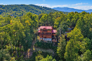 A striking mountain cabin set among lush forest with dramatic Blue Ridge peaks stretching across the horizon.