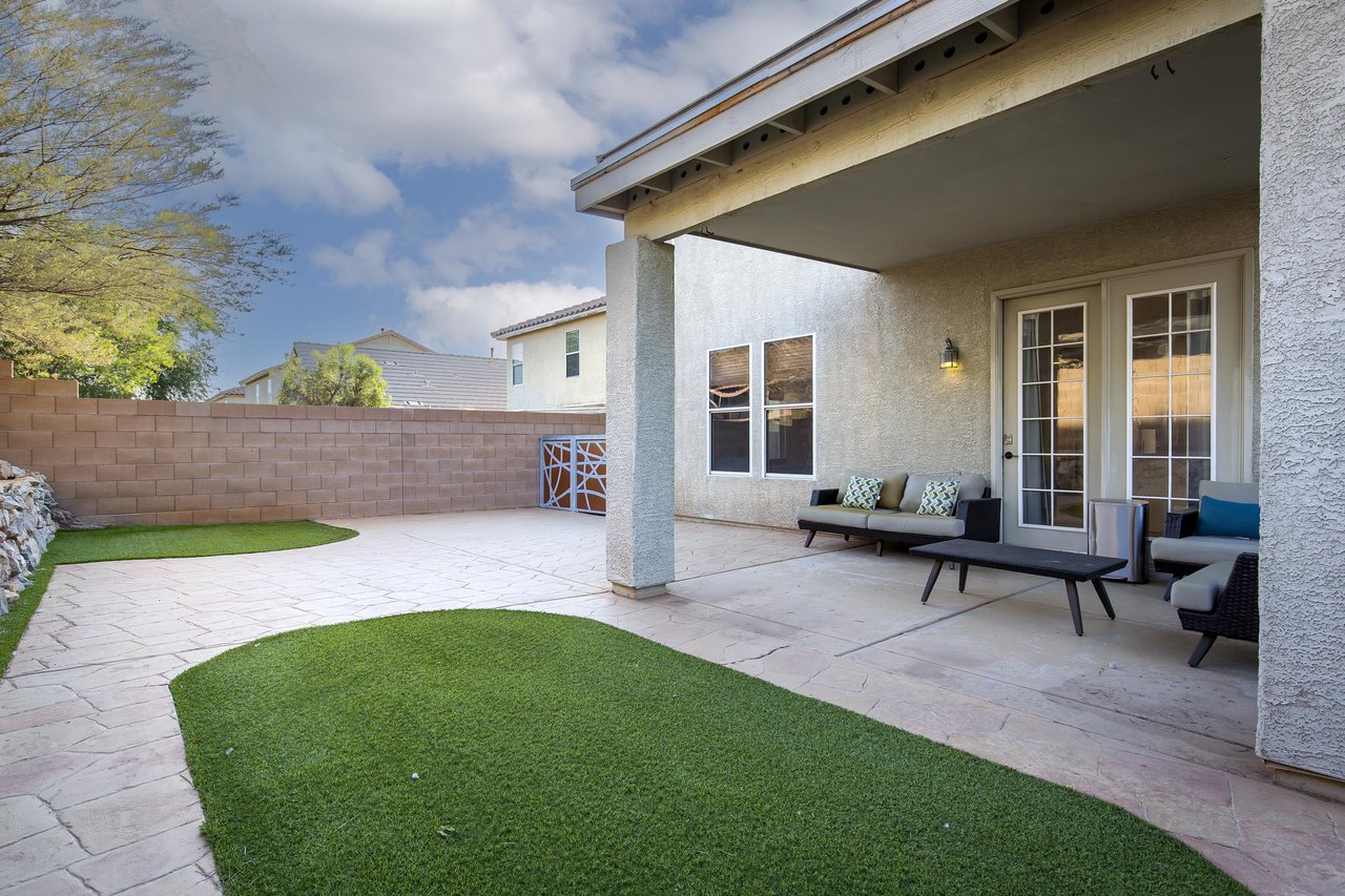 Fully fenced, spacious yard with patio, outdoor seating, and turf grass.