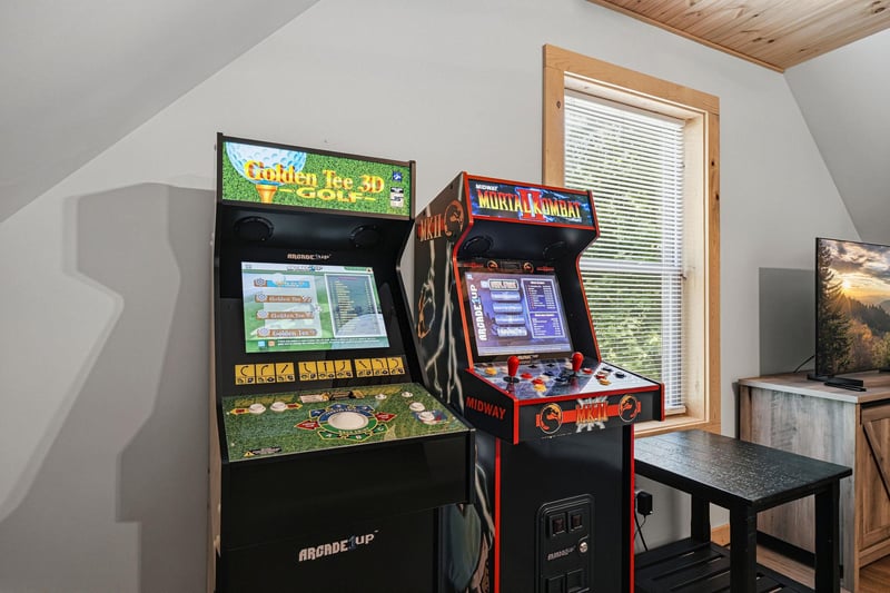 Your private game room awaits with classic arcade machines ready for friendly competition, framed by natural light and cozy woodbeam ceilings overhead.