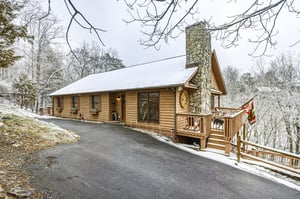 Charming log cabin nestled among snowdusted trees, featuring a stone chimney and welcoming deck for your mountain getaway.