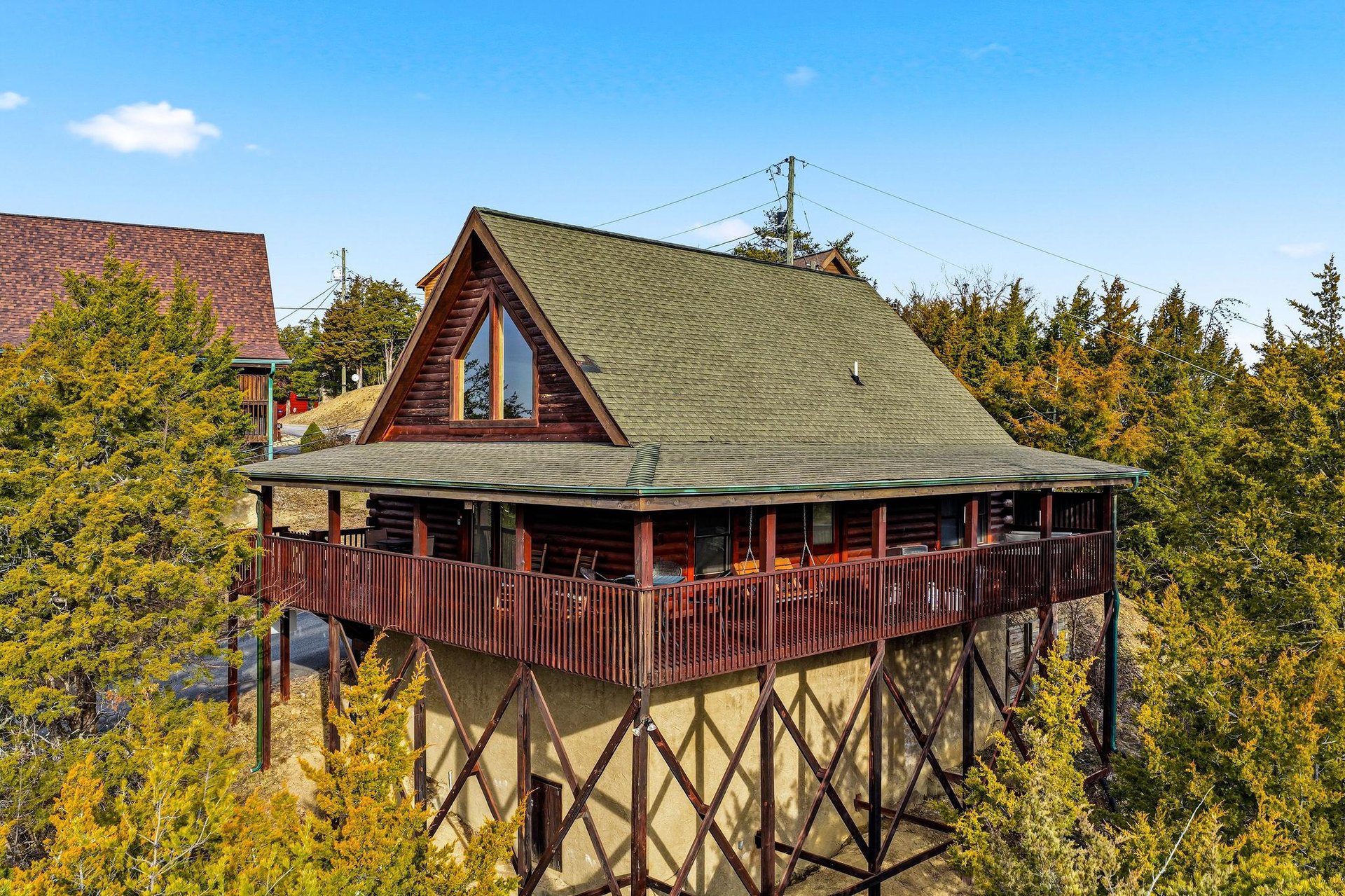 Elevated cabin nestled among towering trees, featuring wraparound deck and mountain architecture in a peaceful forest setting.