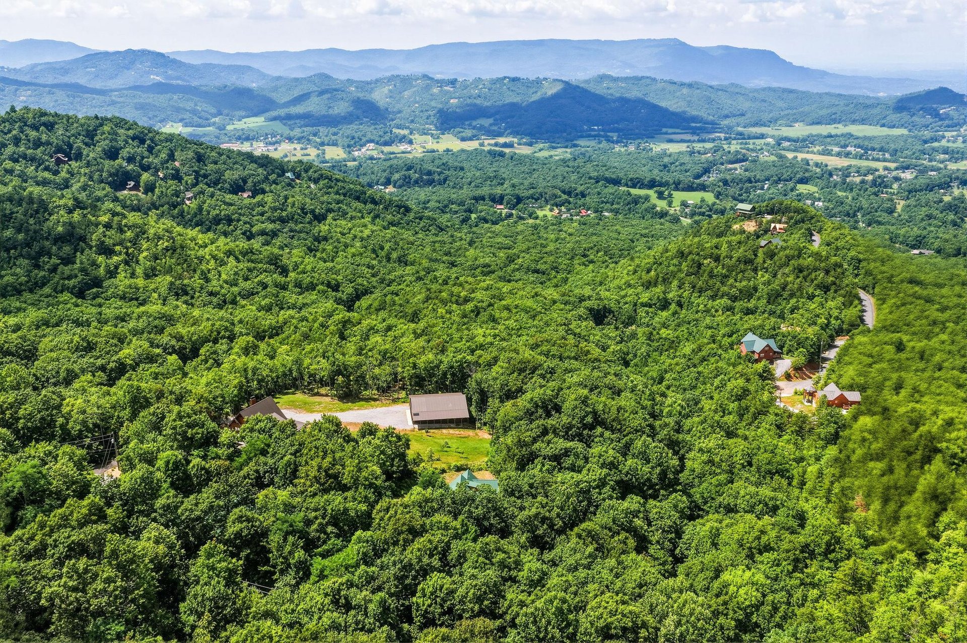Aerial view showcasing the property nestled among lush forested hills with sweeping mountain ranges stretching across the horizon.