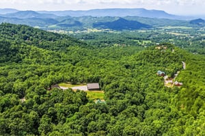 Aerial view showcasing the property nestled among lush forested hills with sweeping mountain ranges stretching across the horizon.