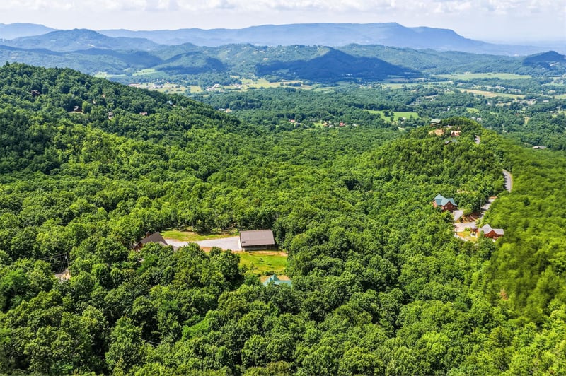 Aerial view showcasing the property nestled among lush forested hills with sweeping mountain ranges stretching across the horizon.