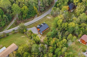 Aerial view of a secluded cabin retreat nestled among lush forest and neighboring properties, accessible via a winding country road.