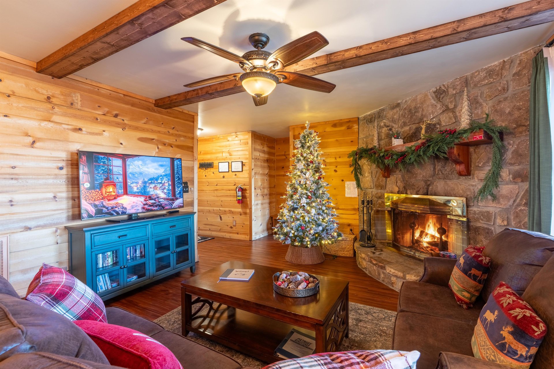 Curl up by the stone fireplace in your cozy mountain living room, where rustic wood beams frame festive holiday décor and every detail invites relaxation.