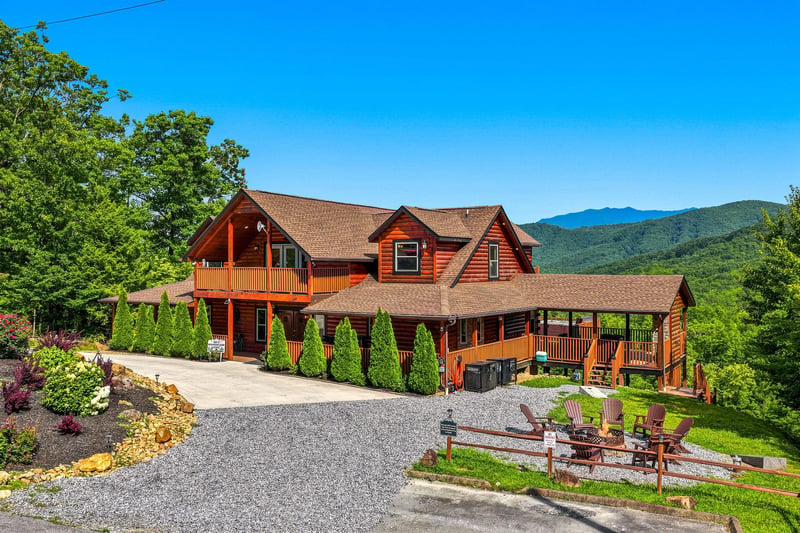 Spacious mountain cabin with wraparound decks, scenic views, and multiple outdoor seating areas, surrounded by lush greenery and rolling hills.