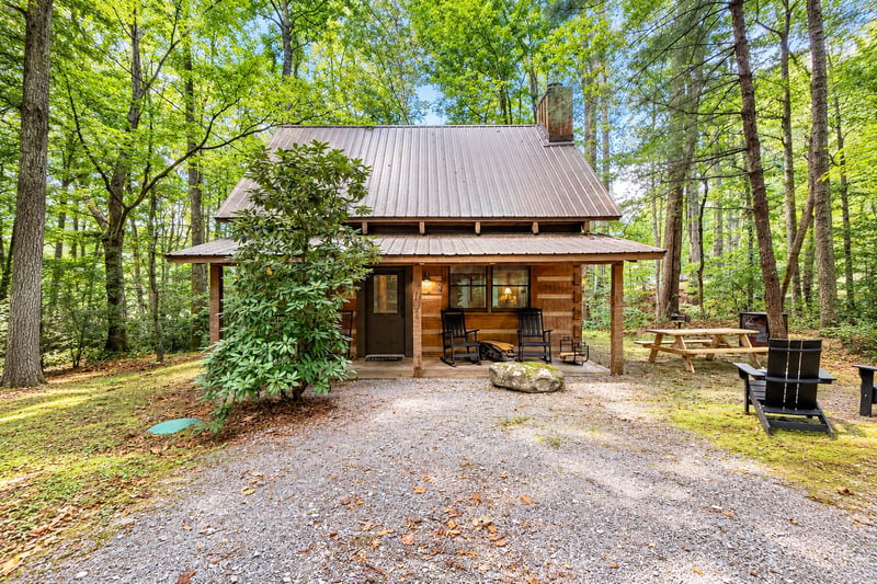A charming wood cabin nestled in the forest, featuring a front porch with rocking chairs, picnic area, and fire pit—perfect for unwinding after a day of adventure.