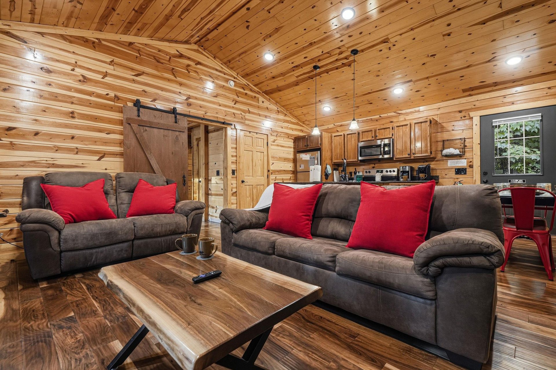Unwind in this beautifully crafted cabin with warm wood tones throughout. Sink into plush seating adorned with bright red pillows, while the rustic barn door and handcrafted coffee table add charming 