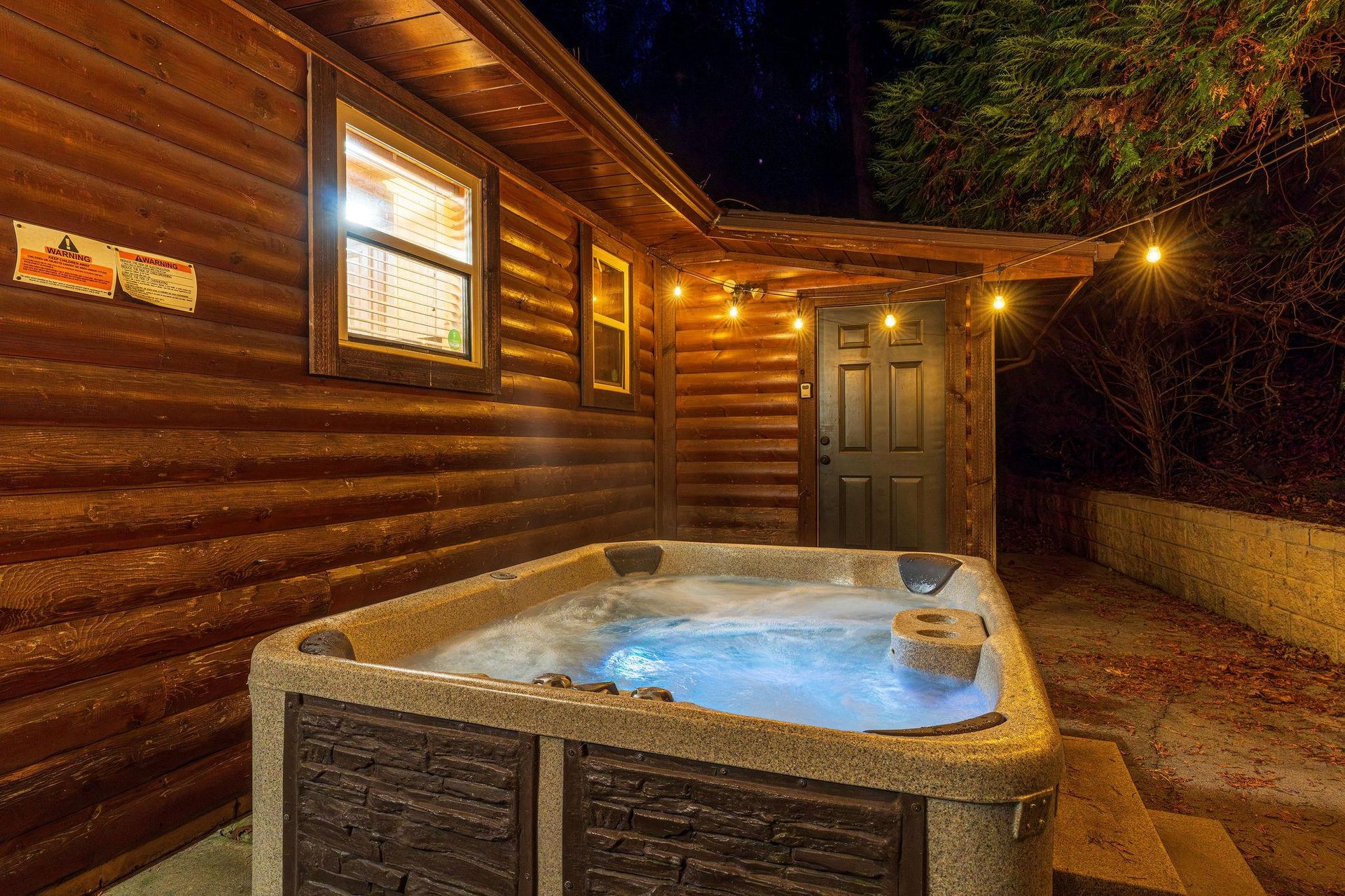 Step into your private hot tub under a starry night sky, surrounded by towering pines. The warm, bubbling water invites you to relax after a day of mountain adventure, while soft cabin lights glow beh