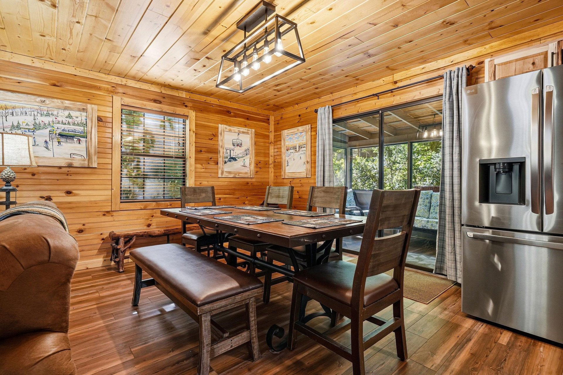 Gather around this rustic dining table where woodplank walls and vaulted ceilings set a cozy cabin mood. Your meals feel warm and inviting, with nature views framed through the large glass doors.