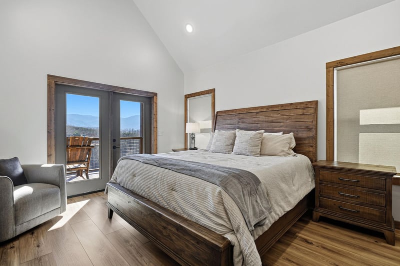 Relax in your cozy bedroom featuring rustic wood accents, crisp linens, and stunning mountain views through French doors leading to your private balcony.