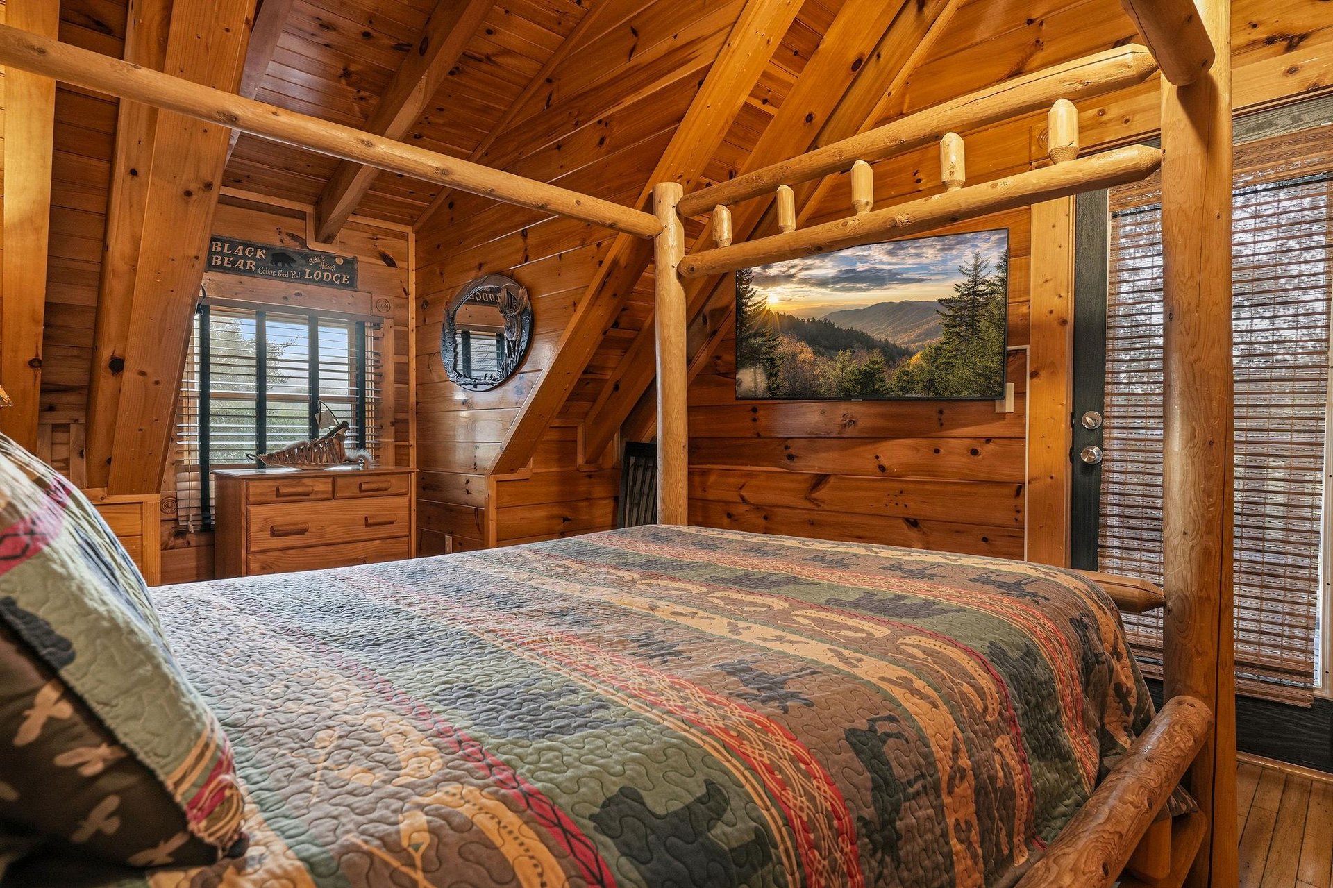 Your rustic retreat features a handcrafted log bed beneath soaring woodbeam ceilings, with a flatscreen TV displaying mountain views to enhance your cozy cabin experience.