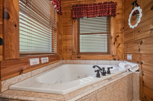 Sink into warmth in your private jetted tub, where rustic cabin charm meets pure relaxation. Sunlight filters through the blinds as fluffy towels await your soak.