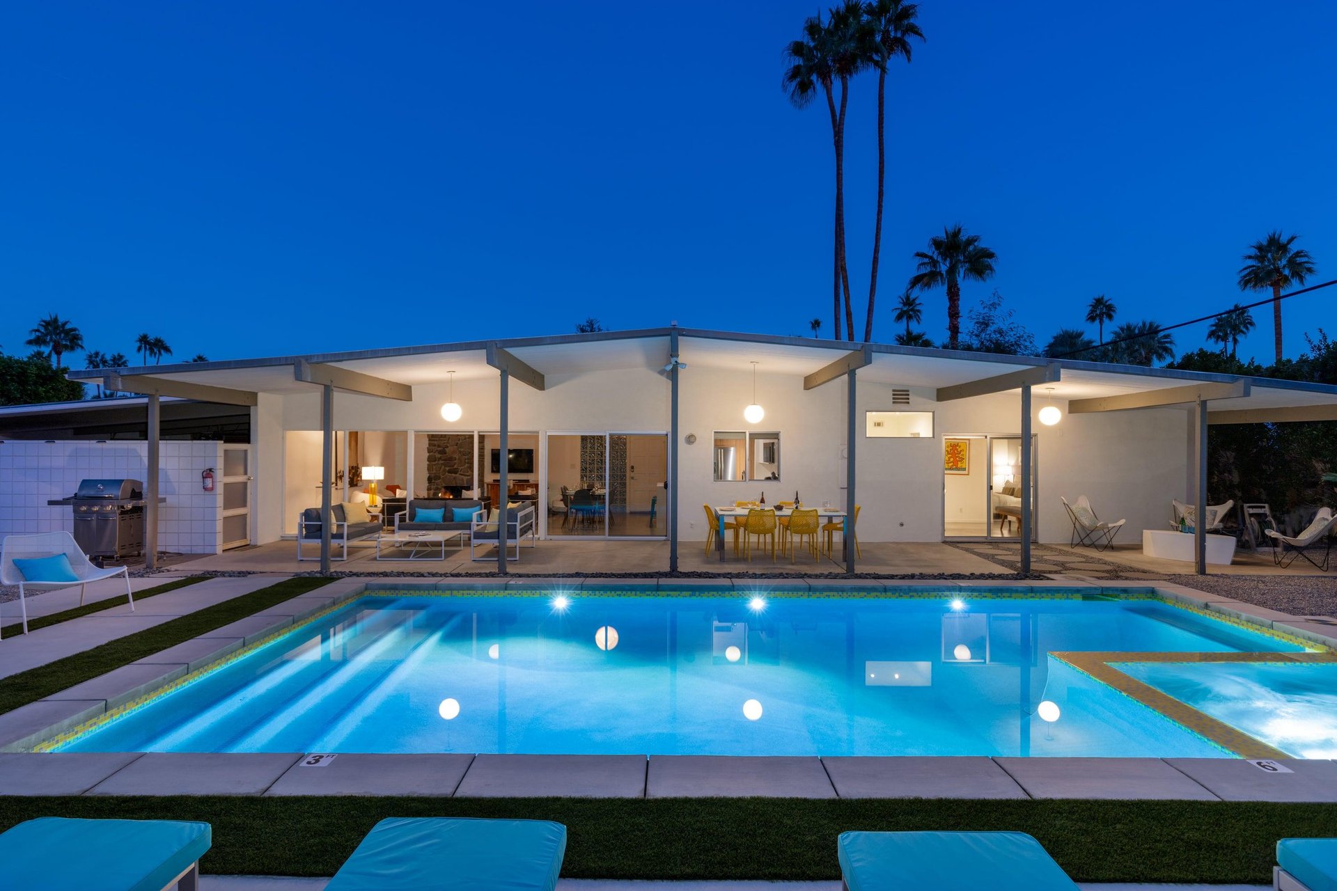 Modern desert retreat featuring a stunning illuminated pool beneath towering palms and starlit skies.
